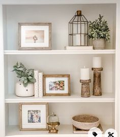 a shelf with pictures, candles and other items on it in a room that has white walls