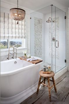 a white bath tub sitting next to a wooden stool in front of a glass shower door