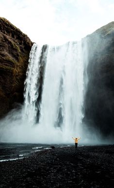 a person standing in front of a waterfall with their arms spread out and hands raised