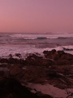 an ocean view with waves crashing on the rocks and pink sky in the back ground