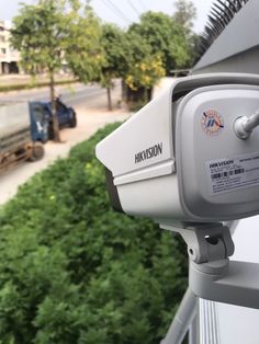 the security camera is attached to the side of a building near a street and trees