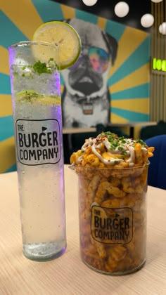 a drink and some food on a table in front of a burger company advertisement wall