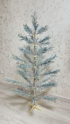 a small blue christmas tree sitting on top of a wooden floor next to a wall