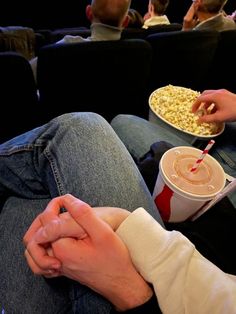 two people are sitting on the couch eating popcorn and drinking sodas while watching movies