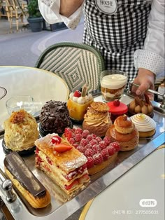 a person in an apron is serving desserts on a tray at a table outside