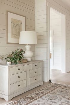 a white dresser sitting next to a lamp on top of a wooden table in a living room