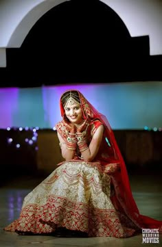 a woman in a red and gold bridal dress sitting on the floor with her hands behind her head