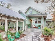 a green house with lots of plants and chairs on the front porch, along with potted trees