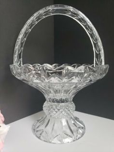 a clear glass basket sitting on top of a white table next to a pink flower