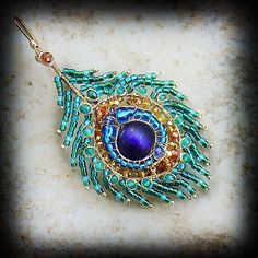 a blue and green broochle with beads hanging from it's side on a marble surface