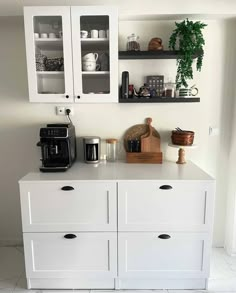 a kitchen with white cupboards and shelves filled with coffee pots, teapots and other items