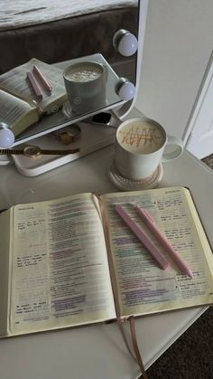 an open book sitting on top of a table next to a coffee cup and pen