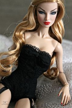 a doll with long blonde hair is laying on the floor wearing a black dress and red nail polish