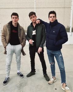 three young men standing next to each other in front of a white building with a brick wall