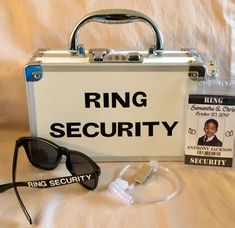 a briefcase, sunglasses and ring security badge on a white sheeted bed with the words ring security