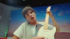 a young man holding an electric guitar in his right hand and making a surprised face