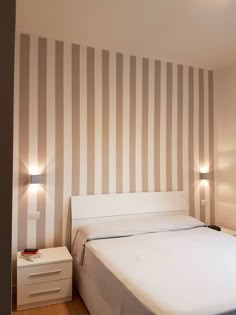 a white bed sitting in a bedroom next to a wall with vertical stripes on it