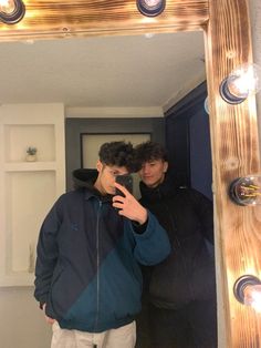 two men standing in front of a mirror taking a selfie