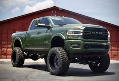 a green ram truck parked in front of a red building with large tires on it