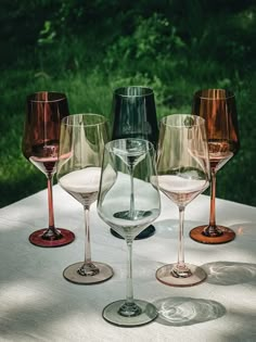 five wine glasses are lined up on a table outside with grass in the back ground