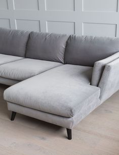 a gray sectional couch sitting on top of a hard wood floor next to a white wall