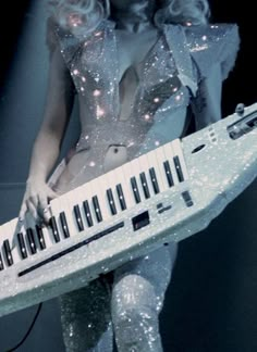 a woman dressed in silver holding a keyboard and wearing tight white clothing with sequins on her body