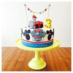 a birthday cake decorated with mickey mouse and paw patrol characters is on a yellow pedestal