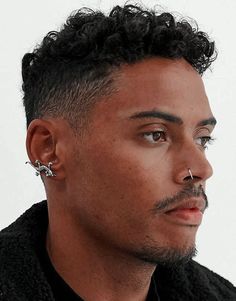 a man with black hair and piercings on his ears looking off to the side