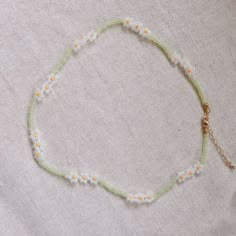 a beaded necklace with daisies and beads on a white cloth covered tablecloth