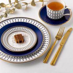 there is a piece of cake on the plate next to a cup of tea and goldware