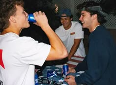 two men are drinking from cans while another man is sitting at a table with an american flag on it