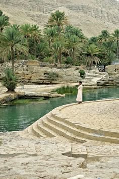 a woman in a white dress standing on steps next to a river and palm trees