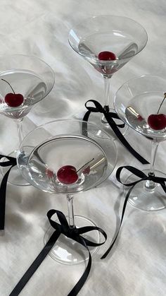 four martini glasses with cherries in them on a white tablecloth, tied with black ribbon