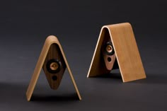 two wooden speakers sitting next to each other on top of a black surface in front of a pair of wood stands