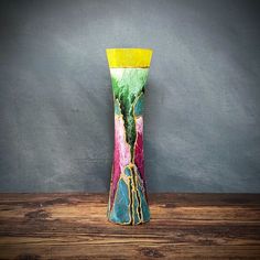 a multicolored vase sitting on top of a wooden table next to a gray wall