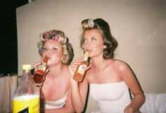 two women sitting next to each other drinking from bottles