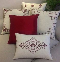 four pillows on a couch with red and white trimmings, one in the shape of a flower