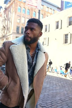 a man in a brown jacket is standing on the street and talking on his cell phone