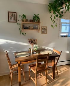 a dining room table and chairs with plants on the wall above it, in front of a window