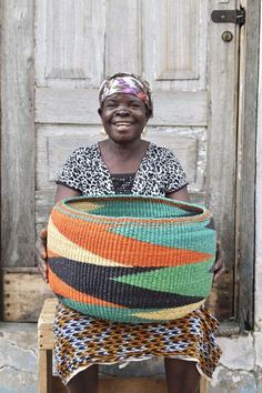 a woman sitting in front of a wooden door holding a large woven basket on her lap