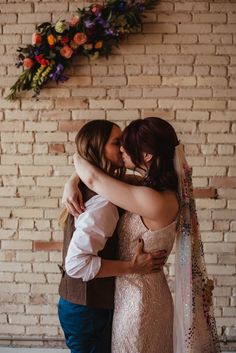 two women hugging each other in front of a brick wall with flowers and garland on it