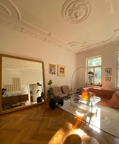 a living room filled with furniture and a large mirror on top of a hard wood floor