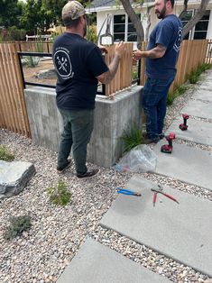 two men are working on an outdoor water feature in their backyard, one is holding the other's hand