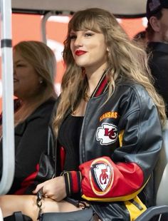 a woman sitting in the stands at a football game wearing a black jacket and red pants