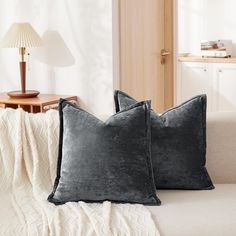 two black velvet pillows sitting on top of a white couch