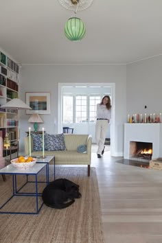 a woman standing in a living room next to a fire place and a dog laying on the floor