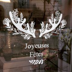 a glass sign with the words joyeus fetes and flowers on it in front of a window