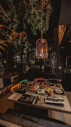 a dining table with food on it in a dark room at night, next to a birdcage hanging from the ceiling