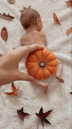 a person holding a pumpkin in the air with leaves scattered around it on a towel