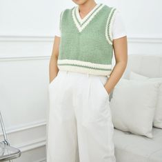 a woman standing in front of a couch wearing white pants and a green knitted sweater